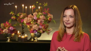 Kristin von festlicher mit roter Bluse vor einem mit Blumen und Kerzen dekoriertem Hintergrund im Interview bei mdr