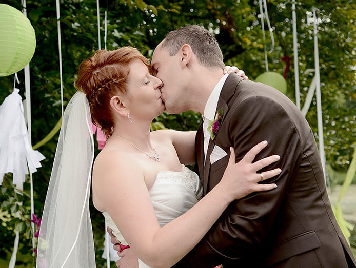 Brautpaar küsst sich - Dekoration und Bäume im Hintergrund