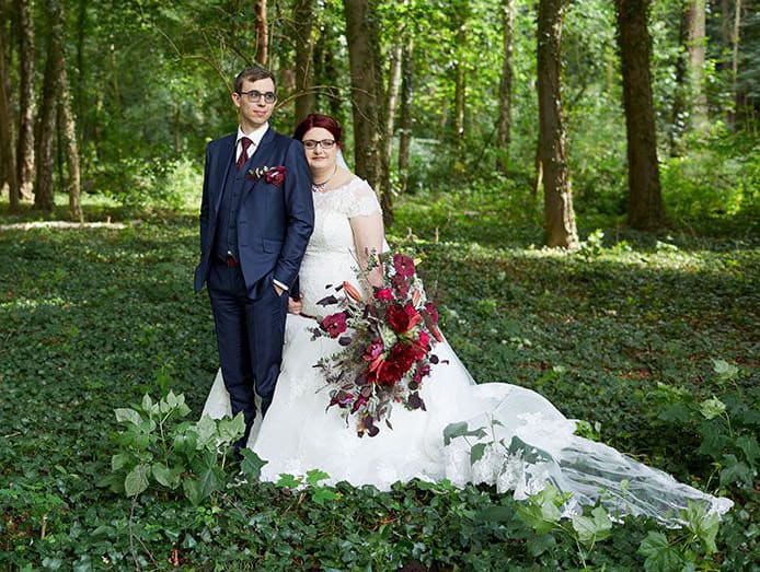 Brautpaar steht aneinandergelehnt in einem Wald