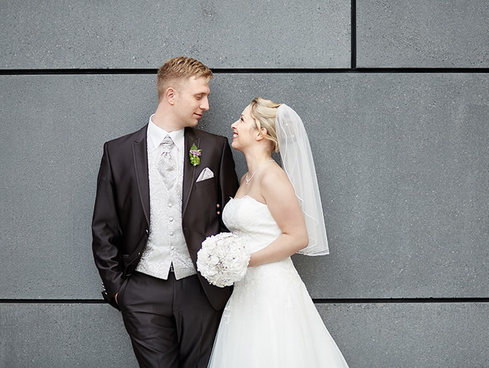 Brautpaar blickt und lächelt sich vor einer grauen Mauer an