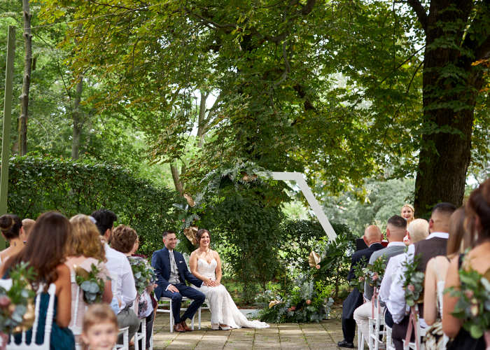 Schloss Breitenfeld Leipzig Außenbereich mit Brautpaar im Hintergrund sitzend vor viel Grün und den Hochzeitsgästen im Vordergrund