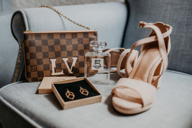 Louis Vuitton Clutch, Ohrringe, Chanel No 5 Parfum & zwei Schuhe auf einem grauen Sessel