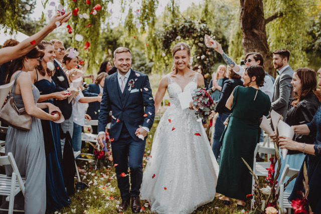 Brautpaar läuft durch einen Blumenregen, den die Gäste von links und rechts werfen