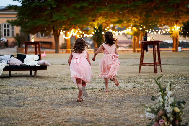 Zwei Mädchen in rosa farbenen Kleidchen rennen in der Dämmerung in Richtung der Hochzeitslocation bzw. zu den brennenden Lichtern