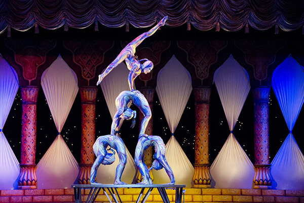 Vier Akrobaten in reflektierenden Anzügen zeigen eine Figur in einem Theater